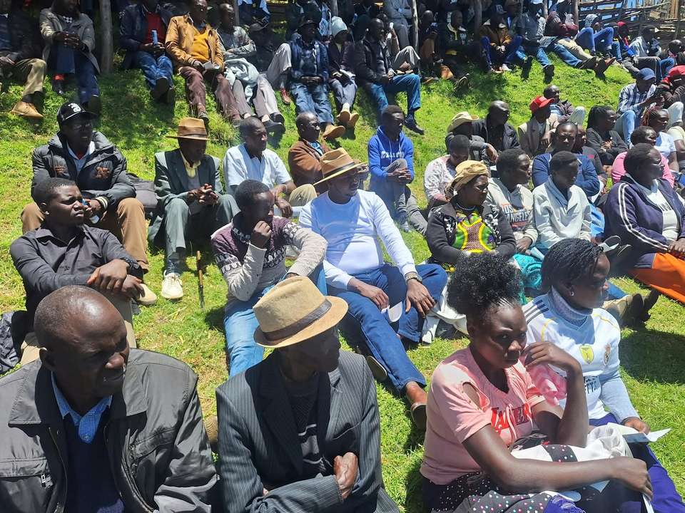 Young people, women and elders seated together on a hillside at a community meeting