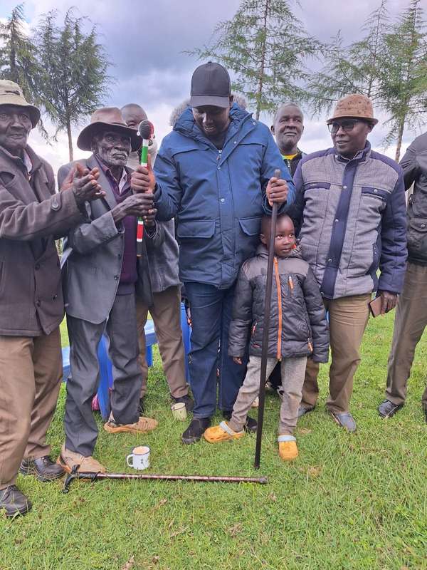 Long’ole in a blue jacket and cap with elders and a small child, holding a beaded staff
