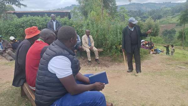 Long’ole, notebook in hand, listens as an elder speaks at an outdoor meeting