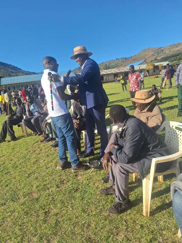 Long’ole greets a young man at a gathering on a school field, hills behind