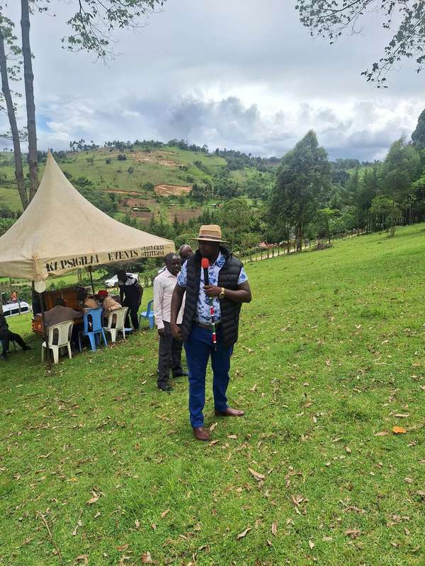 Long’ole speaks into a microphone on a green field with hills behind