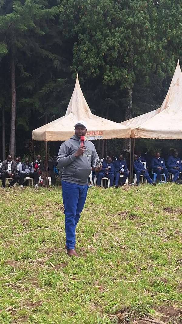 Long’ole in a grey hoodie and white cap speaks into a microphone in front of tents
