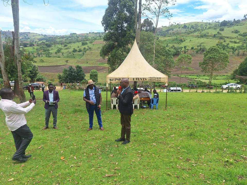 A community meeting on a green valley floor, with farmland and hills behind
